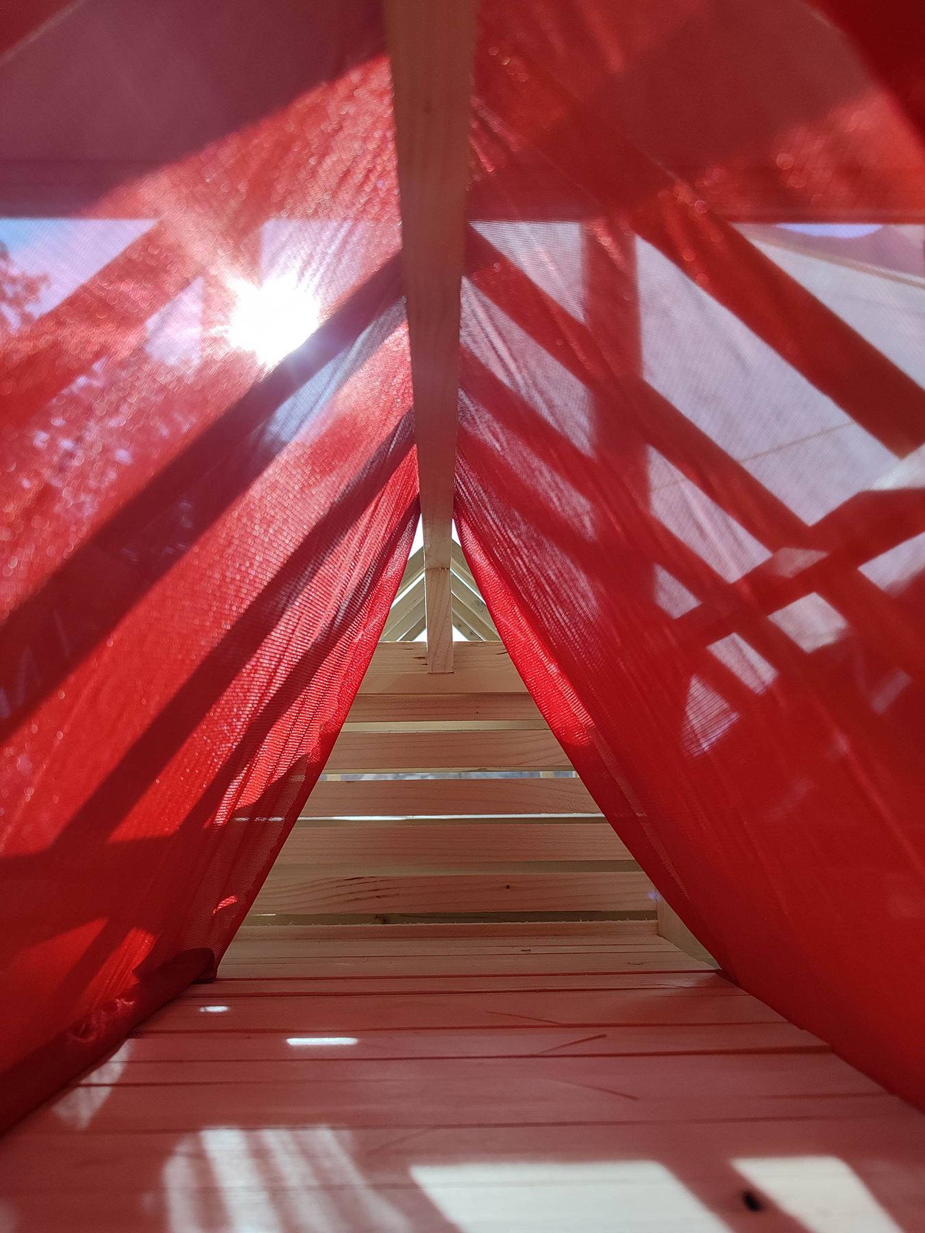 Roter Stoff in einer Holzkonstruktion durch die die Sonne hinein scheint