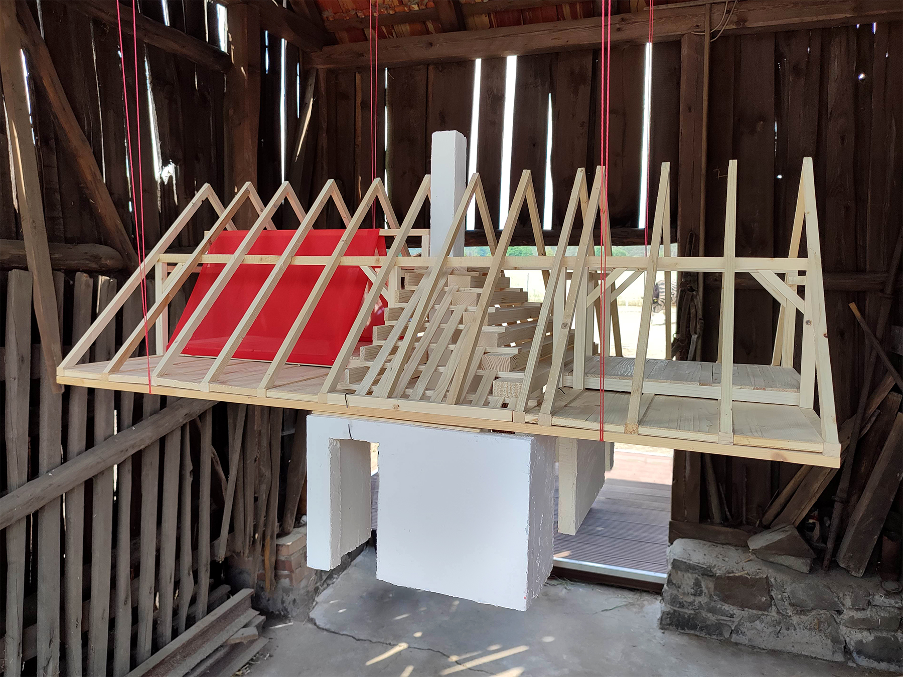 Holzmodell eines Daches das an Schnüren in einer alten Scheune hängt
